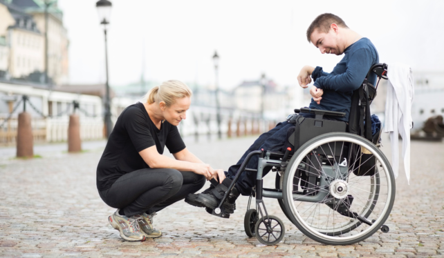 Young woman helping a man in a wheelchair by tying his shoe lace