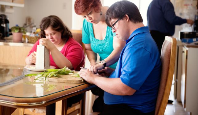 Woman teaching two people to cut vegetables and grate cheese